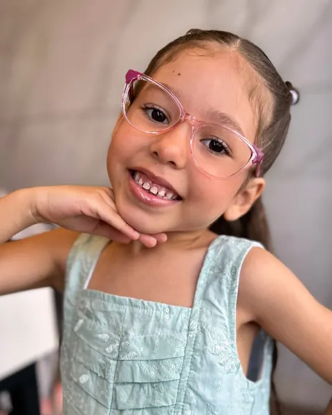 Menina sorrindo com óculos de armação rosa transparente