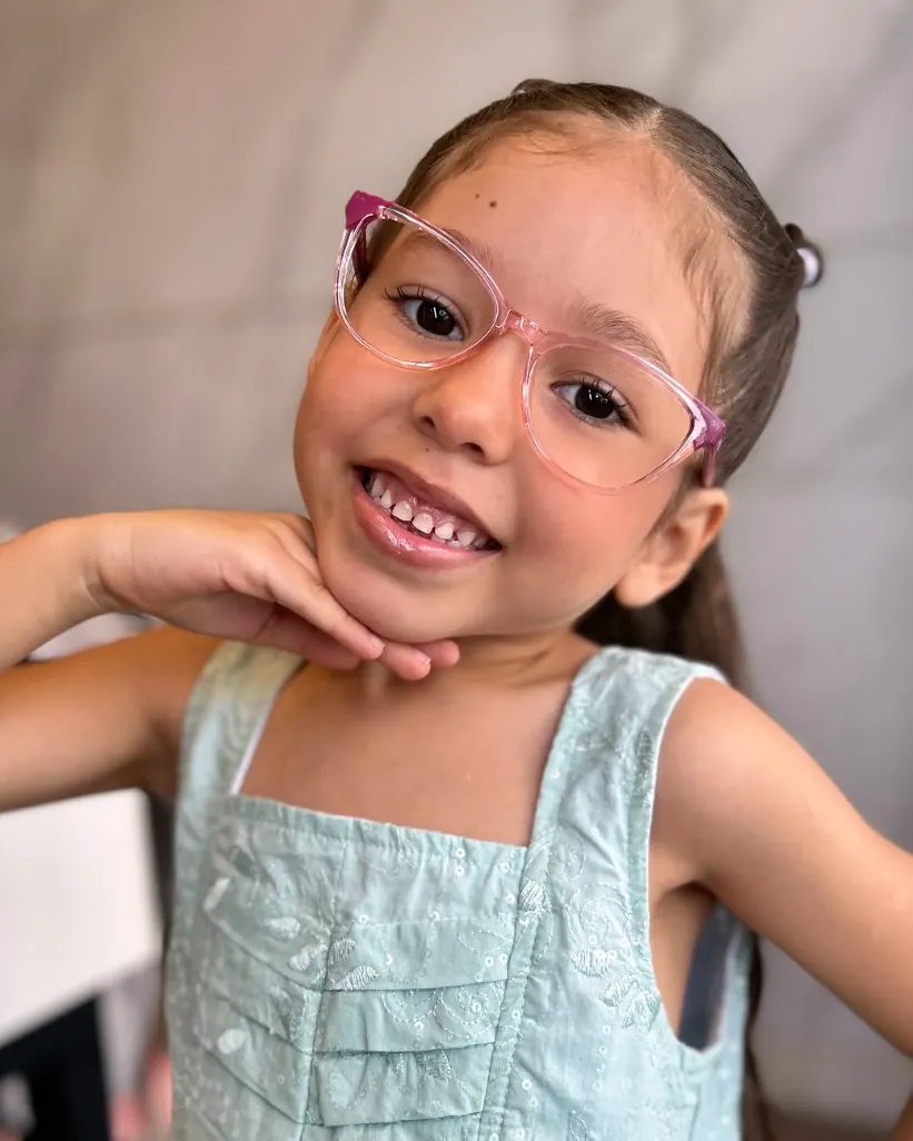 Menina sorrindo com óculos de armação rosa transparente